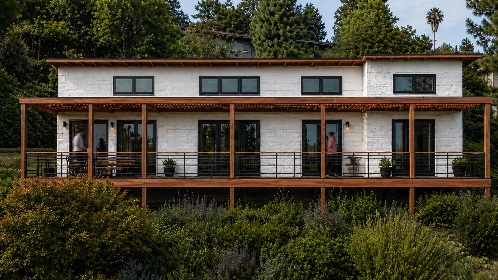 Front elevation of ADU 04 with a long white facade and timber porch in a planted garden